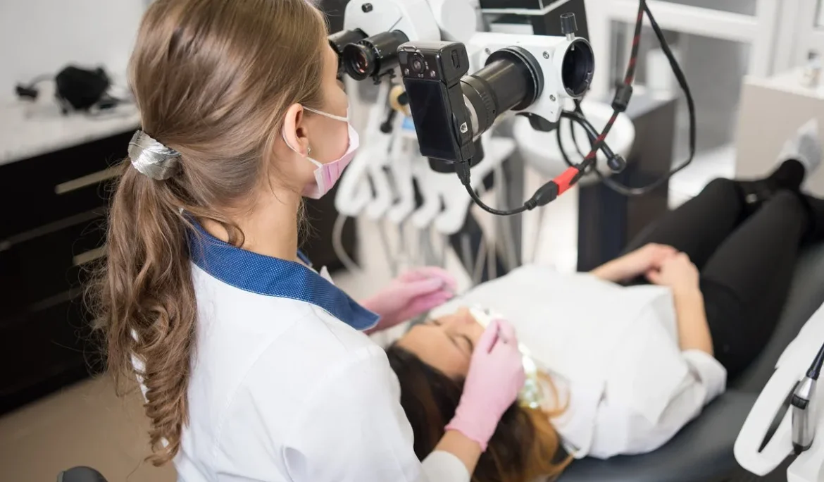 Female dentist with dental tools - microscope, mirror and probe checking up patient teeth at dental clinic office. Medicine, dentistry and health care concept. Dental equipment